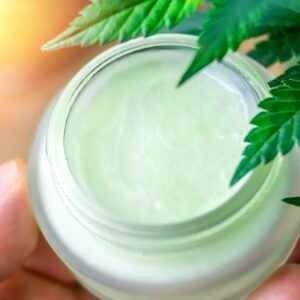 Hand holding Cannabis CBD lotion cream against Marijuana plant
