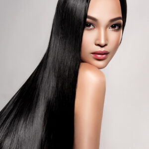 Black haired young woman with asian appearance is demonstrating dense, well cared, straight hair. Asian beauty.