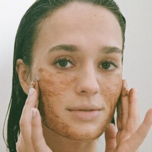 Woman applying coffee scrub to her face to exfoliate dead skin cells.